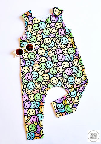 handmade baby dungarees made in a brightly coloured 90's smiley face design. Photographed with kids cream retro sunglasses